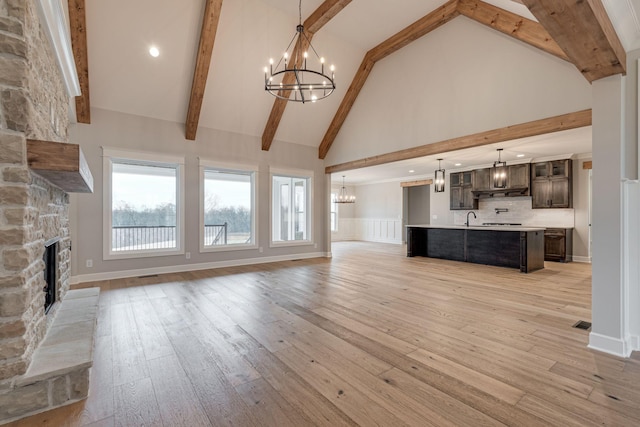 unfurnished living room featuring a stone fireplace, beamed ceiling, high vaulted ceiling, and light wood-type flooring