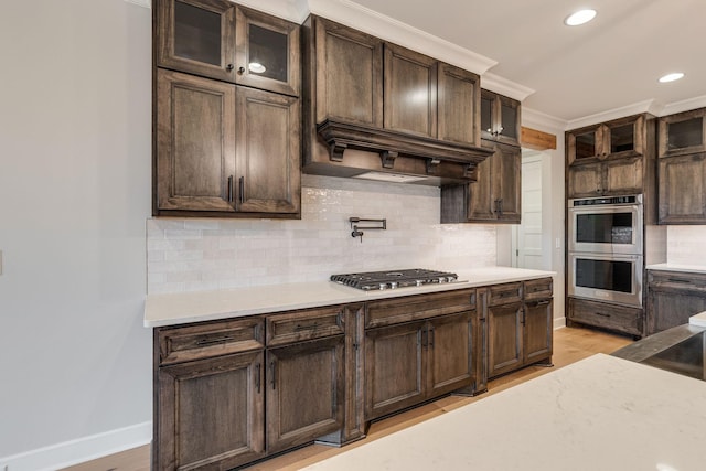 kitchen featuring appliances with stainless steel finishes, backsplash, dark brown cabinetry, crown molding, and light hardwood / wood-style floors