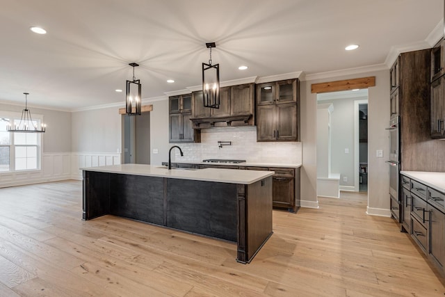 kitchen featuring a center island with sink, sink, light wood-type flooring, dark brown cabinetry, and stainless steel appliances