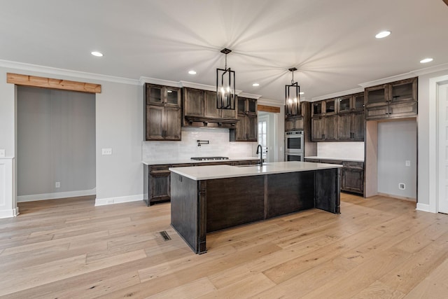 kitchen featuring dark brown cabinets, light hardwood / wood-style flooring, ornamental molding, and an island with sink