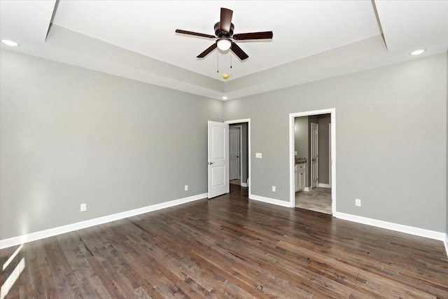 unfurnished bedroom featuring ensuite bathroom, a raised ceiling, ceiling fan, and dark wood-type flooring