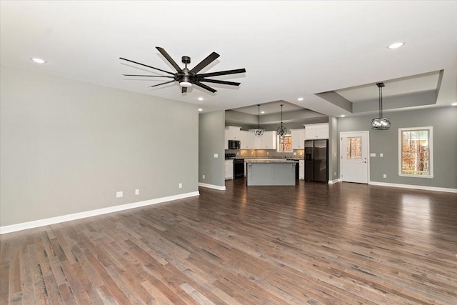 unfurnished living room featuring a raised ceiling, ceiling fan, and dark hardwood / wood-style flooring