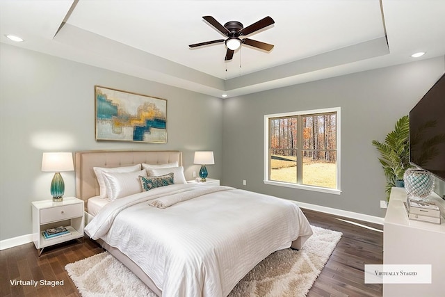 bedroom featuring dark hardwood / wood-style floors, ceiling fan, and a tray ceiling