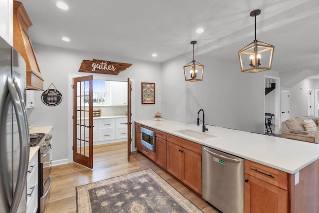 kitchen with appliances with stainless steel finishes, sink, pendant lighting, light hardwood / wood-style flooring, and a chandelier