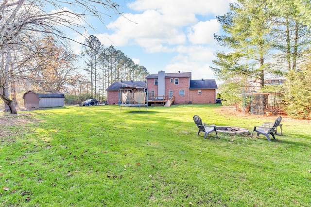 view of yard featuring a trampoline, a storage unit, a deck, and an outdoor fire pit