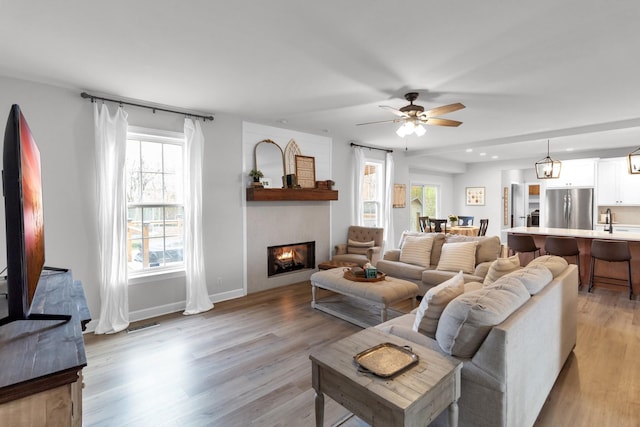 living room with a fireplace, ceiling fan, plenty of natural light, and light wood-type flooring