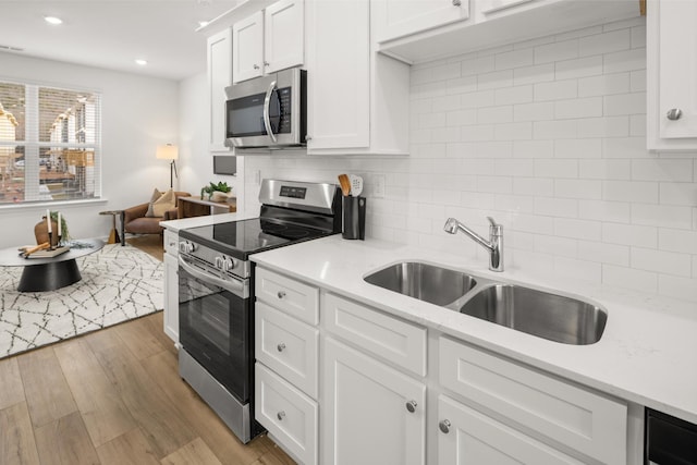 kitchen featuring backsplash, white cabinets, sink, light wood-type flooring, and appliances with stainless steel finishes