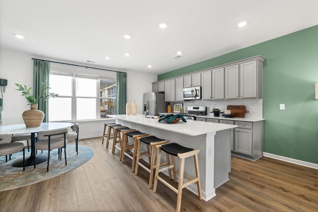 kitchen featuring gray cabinetry, a breakfast bar, stainless steel appliances, hardwood / wood-style floors, and an island with sink