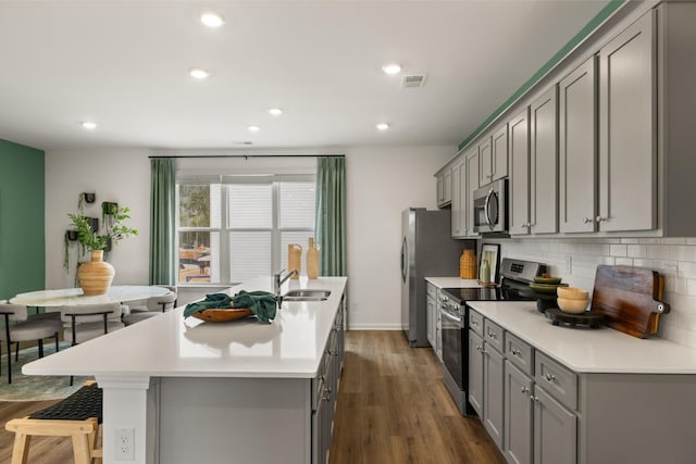 kitchen with gray cabinetry, a center island with sink, sink, tasteful backsplash, and stainless steel appliances