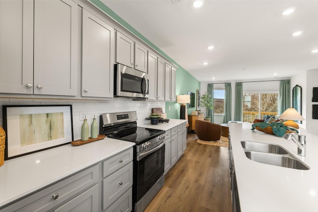 kitchen with sink, tasteful backsplash, dark hardwood / wood-style floors, gray cabinets, and appliances with stainless steel finishes