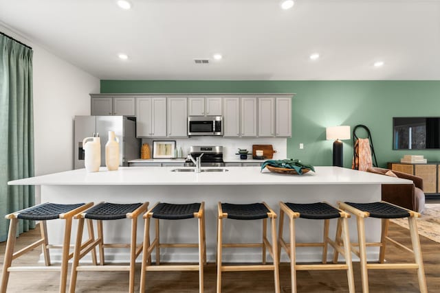 kitchen with a large island with sink, sink, appliances with stainless steel finishes, and light hardwood / wood-style flooring