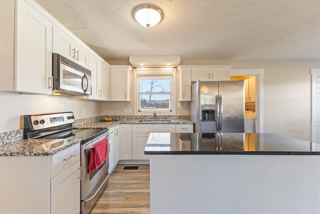 kitchen with light wood-type flooring, stainless steel appliances, sink, dark stone countertops, and white cabinets