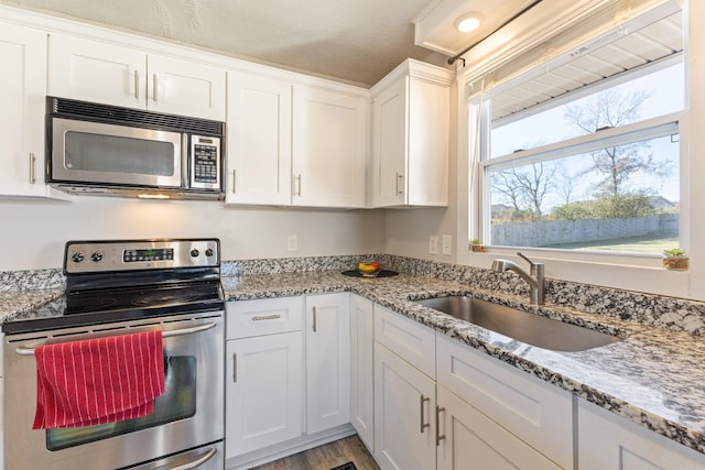 kitchen with light stone counters, white cabinetry, sink, and appliances with stainless steel finishes