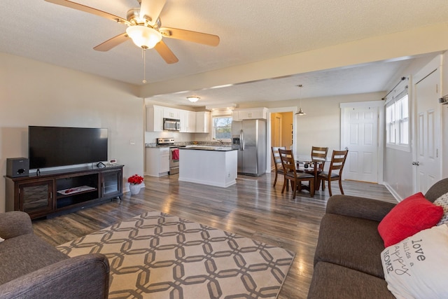 living room with a textured ceiling, ceiling fan, and dark wood-type flooring