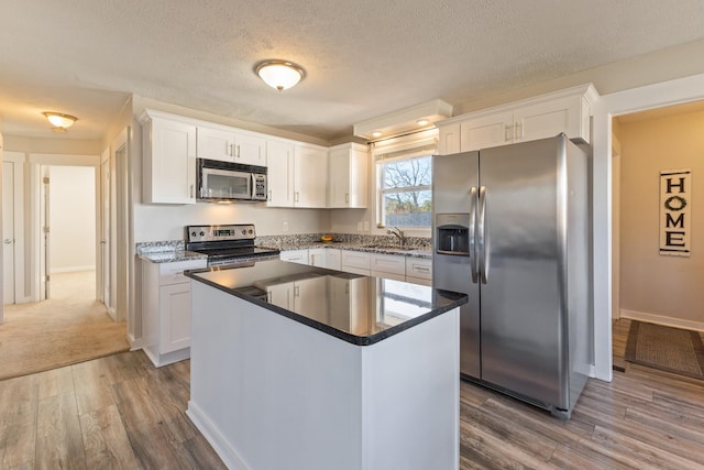 kitchen featuring hardwood / wood-style floors, white cabinets, a textured ceiling, and appliances with stainless steel finishes