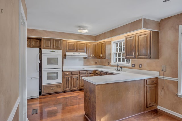 kitchen featuring hardwood / wood-style floors, kitchen peninsula, white appliances, and sink