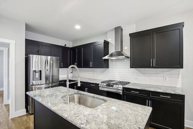 kitchen with sink, stainless steel appliances, wall chimney range hood, hardwood / wood-style floors, and an island with sink