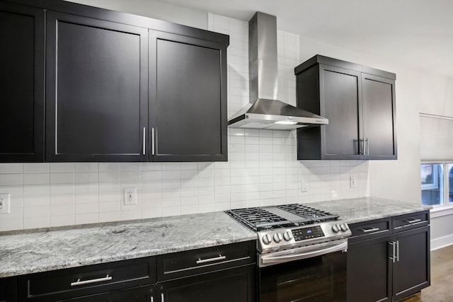 kitchen featuring backsplash, stainless steel gas range, hardwood / wood-style flooring, wall chimney exhaust hood, and light stone countertops