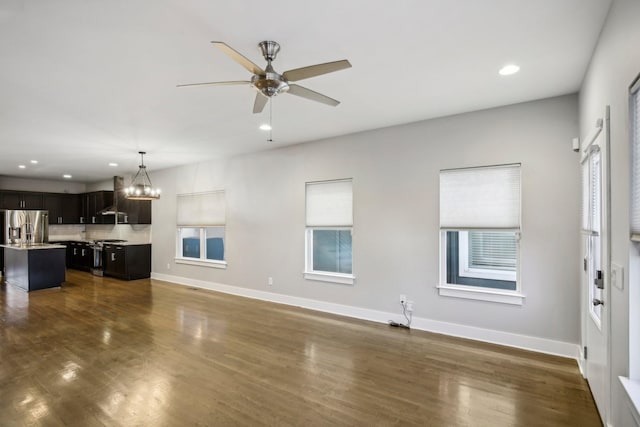 unfurnished living room featuring ceiling fan with notable chandelier and dark hardwood / wood-style flooring