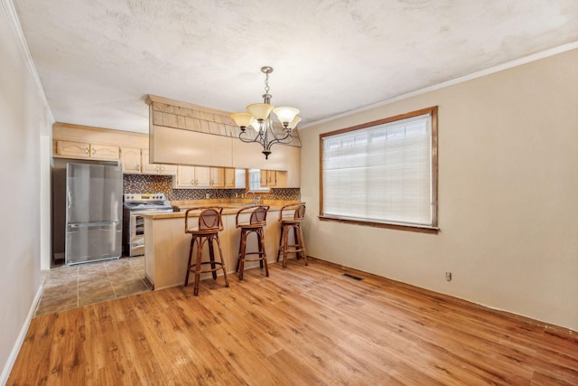 kitchen with a kitchen breakfast bar, appliances with stainless steel finishes, decorative light fixtures, light hardwood / wood-style floors, and kitchen peninsula