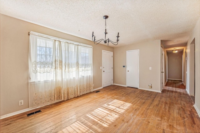 unfurnished dining area with hardwood / wood-style floors, a textured ceiling, and an inviting chandelier