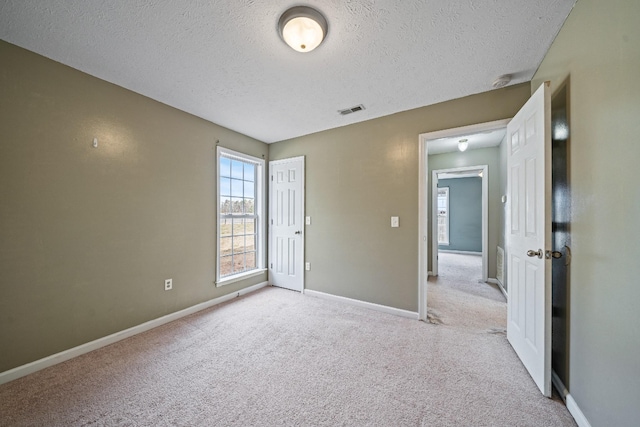 spare room featuring light colored carpet and a textured ceiling