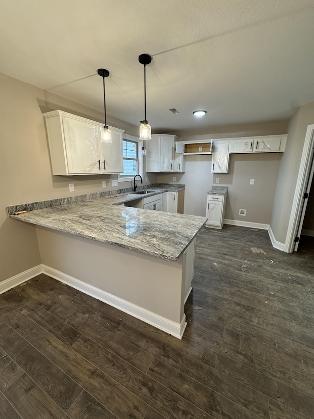 kitchen with a peninsula, baseboards, dark wood-type flooring, and a sink