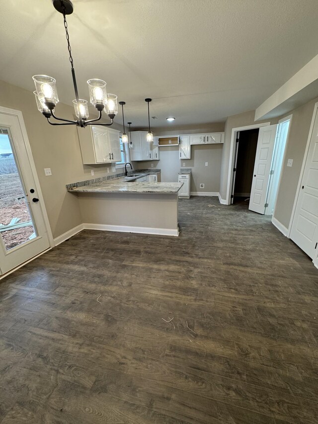 kitchen featuring a peninsula, dark wood-type flooring, a sink, white cabinetry, and baseboards