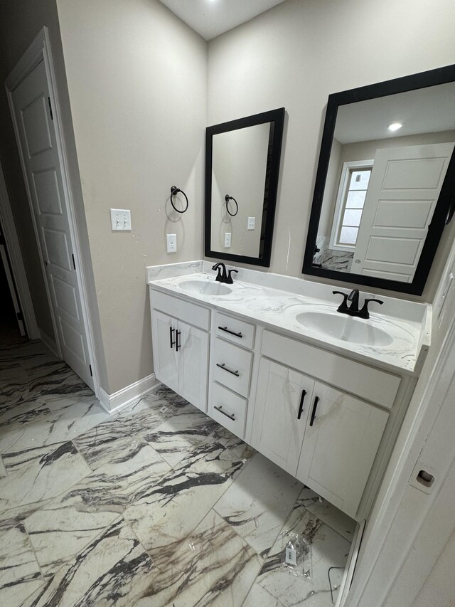 bathroom with double vanity, marble finish floor, baseboards, and a sink