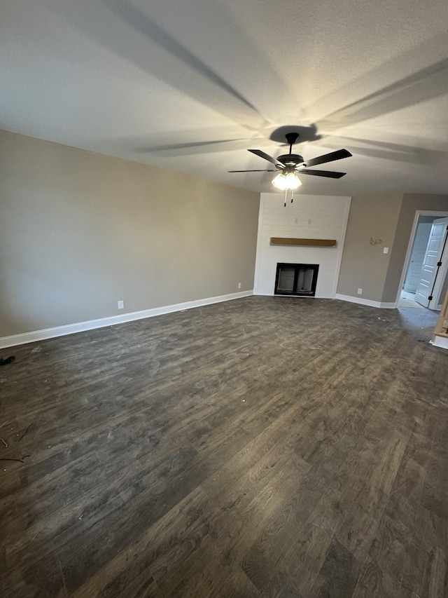 unfurnished living room with a textured ceiling, dark wood-type flooring, a fireplace, a ceiling fan, and baseboards