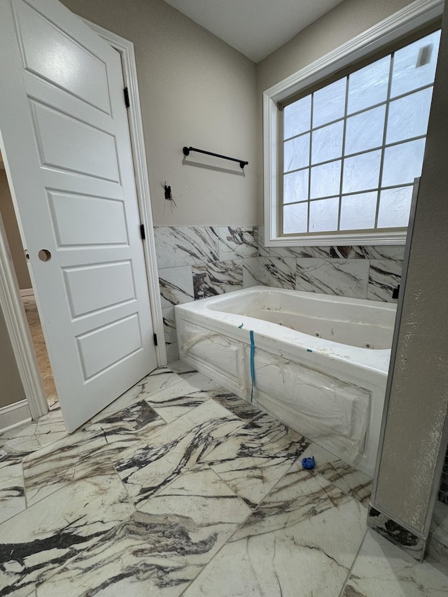 bathroom featuring a wainscoted wall, marble finish floor, a tub with jets, and tile walls