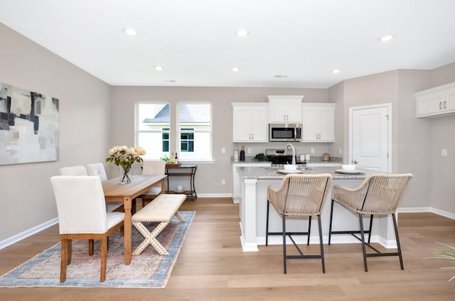 kitchen featuring white cabinets, light hardwood / wood-style floors, a center island with sink, and stainless steel appliances