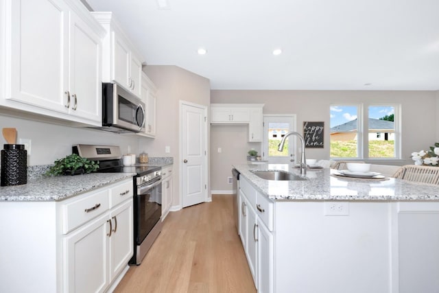 kitchen with sink, stainless steel appliances, a kitchen island with sink, white cabinets, and light wood-type flooring