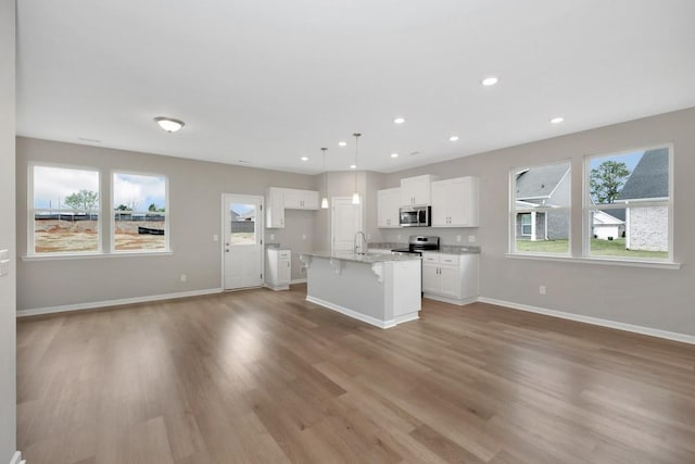 kitchen featuring white cabinetry, stainless steel appliances, pendant lighting, light hardwood / wood-style floors, and a kitchen island with sink