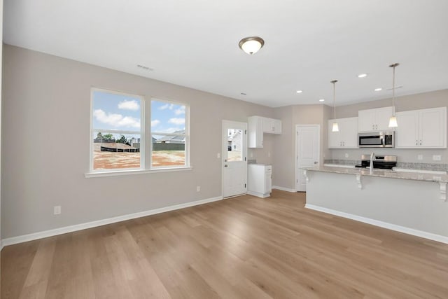 kitchen featuring white cabinets, light hardwood / wood-style flooring, appliances with stainless steel finishes, decorative light fixtures, and light stone counters