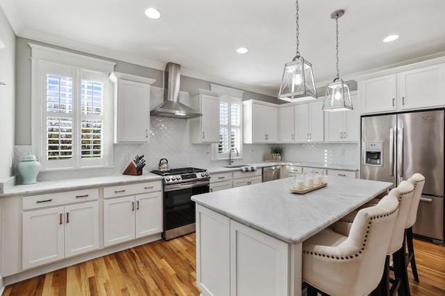 kitchen featuring a healthy amount of sunlight, stainless steel appliances, white cabinetry, and wall chimney exhaust hood