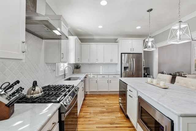 kitchen with stainless steel appliances, wall chimney range hood, light hardwood / wood-style floors, decorative light fixtures, and white cabinets