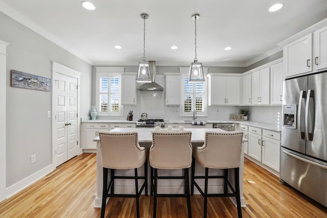 kitchen with white cabinetry, a healthy amount of sunlight, wall chimney range hood, and appliances with stainless steel finishes