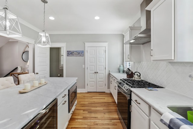 kitchen featuring light wood-type flooring, wall chimney exhaust hood, stainless steel appliances, pendant lighting, and white cabinets