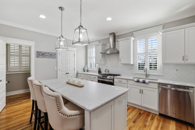 kitchen featuring white cabinets, appliances with stainless steel finishes, a center island, and wall chimney exhaust hood