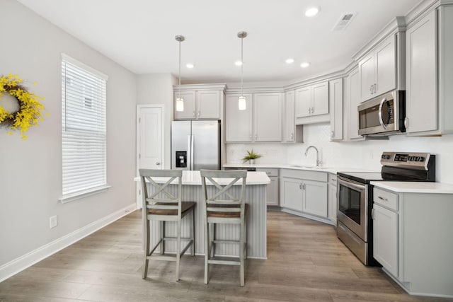 kitchen with light hardwood / wood-style floors, decorative light fixtures, gray cabinets, a kitchen island, and appliances with stainless steel finishes