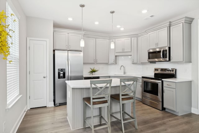 kitchen with gray cabinetry, appliances with stainless steel finishes, pendant lighting, a kitchen island, and light wood-type flooring