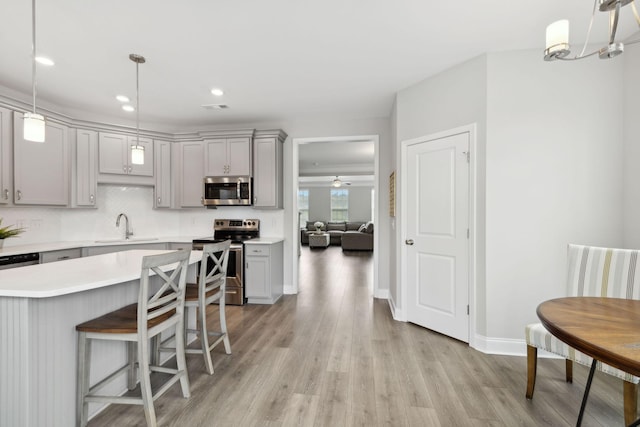 kitchen with light hardwood / wood-style floors, sink, stainless steel appliances, and hanging light fixtures