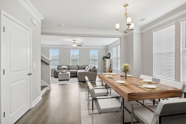 dining space with wood-type flooring, ceiling fan with notable chandelier, and crown molding