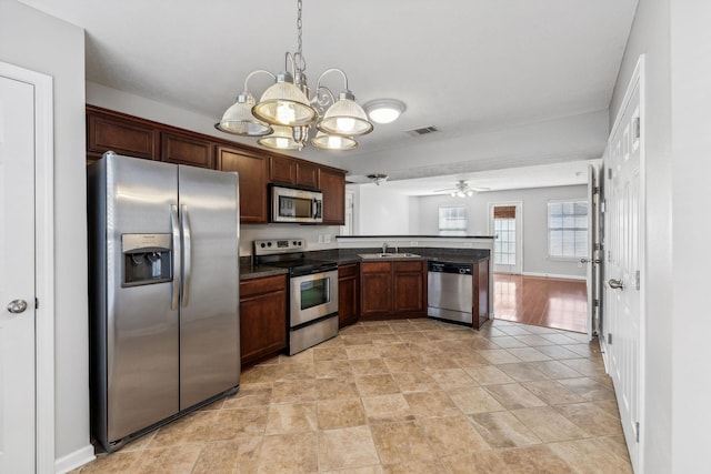 kitchen featuring kitchen peninsula, appliances with stainless steel finishes, ceiling fan with notable chandelier, sink, and hanging light fixtures