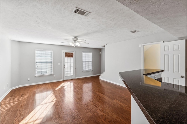 unfurnished living room featuring a textured ceiling, ceiling fan, and dark wood-type flooring