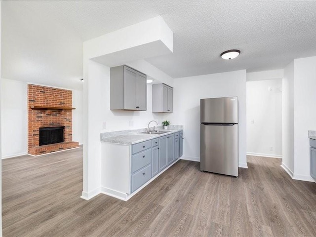 kitchen with light hardwood / wood-style floors, sink, a fireplace, gray cabinets, and stainless steel refrigerator