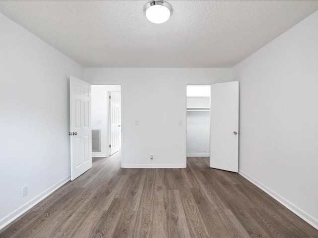 unfurnished bedroom with a spacious closet, a closet, dark wood-type flooring, and a textured ceiling