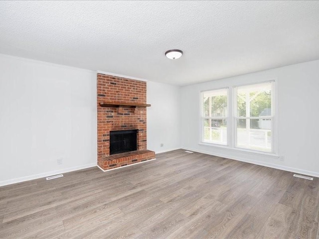 unfurnished living room featuring a brick fireplace, a textured ceiling, and light hardwood / wood-style flooring