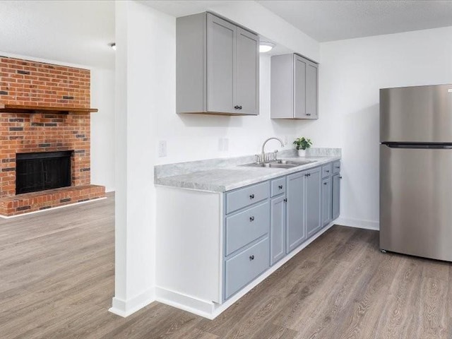 kitchen featuring stainless steel refrigerator, gray cabinetry, sink, a brick fireplace, and light hardwood / wood-style flooring